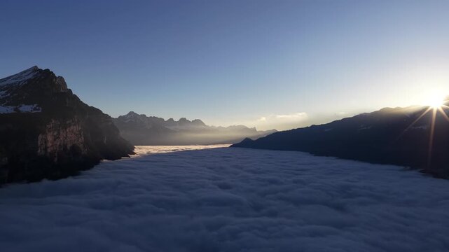 Churfirsten mountains in Switzerland, drone pulling back above sea of clouds, alpine ridges, winter mood, sunrise light and calm atmosphere.