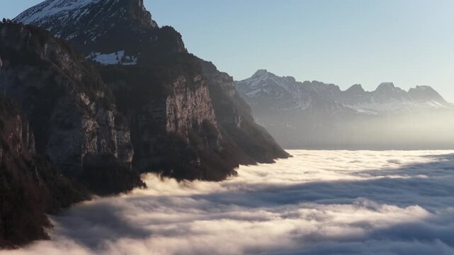 Churfirsten mountains in Switzerland, drone view above sea of clouds, dramatic alpine cliffs, soft morning light and winter atmosphere.
