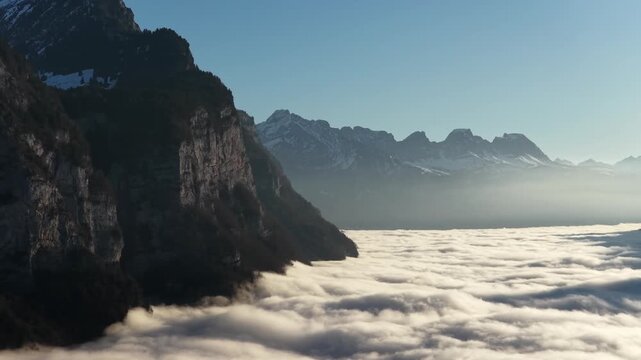 Churfirsten mountains, Switzerland, drone above cloud inversion with dramatic cliffs, soft morning light, alpine peaks and calm atmosphere.