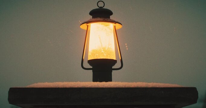 Static Shot of Lamp Post Sitting on Concrete Column Illuminating Yellow Light as Snow Falls During Dusk