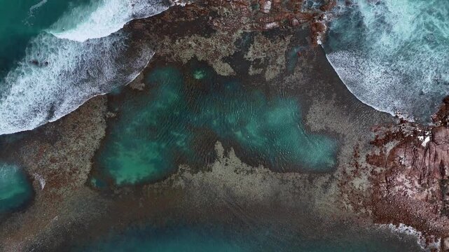 Top down aerial ascend of turquoise water and submerged rocks near Daly Head coastline, natural coral pool, waves and whitewash