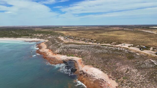 Aerial pullback of rugged cliffs and rocky shoreline extending into the ocean at Daly Head, campers on flat ground