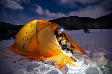 Female camper eating freeze dried food inside illuminated winter tent at night   © XArt