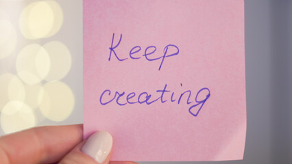 Hand holding pink sticky note with handwritten message in blurred background