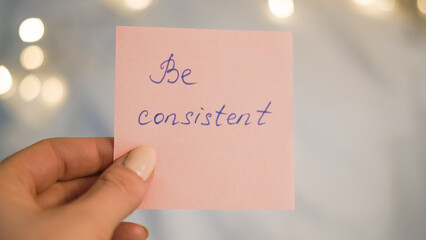 Hand holding pink sticky note with handwritten message on blurred background