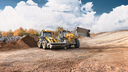 Obraz premium Loaders and excavators are performing earth moving and site preparation at a construction site during the day. The ground is uneven and dusty
