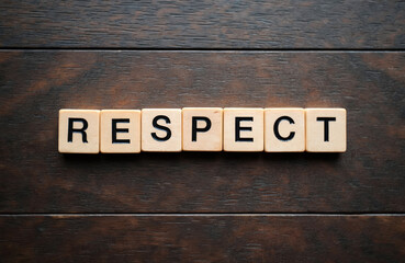 Fototapeta premium Wooden blocks spell the word RESPECT on a dark wood surface. Concept conveys acknowledgement honor and regard for others. Simple graphic text.