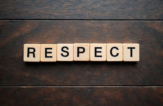 Wooden blocks spell the word RESPECT on a dark wood surface. Concept conveys acknowledgement honor and regard for others. Simple graphic text.