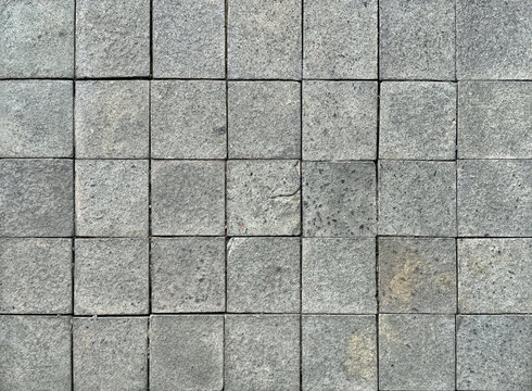 Square grey paving outdoor stone tiles with random shades and roughness. Suitable for exterior garden flooring. Seamless background texture.