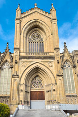 Obraz premium Detail shot of the portico and main facade of the Cathedral of Mary Immaculate in Vitoria Gasteiz, featuring neo gothic stone architecture, arches and ornamental details under a blue sky. 