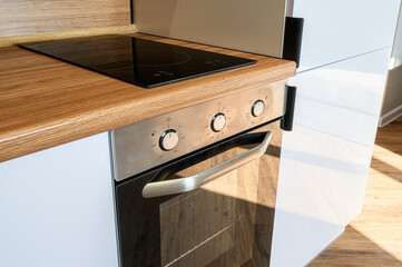 modern kitchen setup with a black induction hob, stainless steel oven with three knobs, wooden...