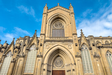 Detail shot of the portico and main facade of the Cathedral of Mary Immaculate in Vitoria Gasteiz, featuring neo gothic stone architecture, arches and ornamental details under a blue sky. 