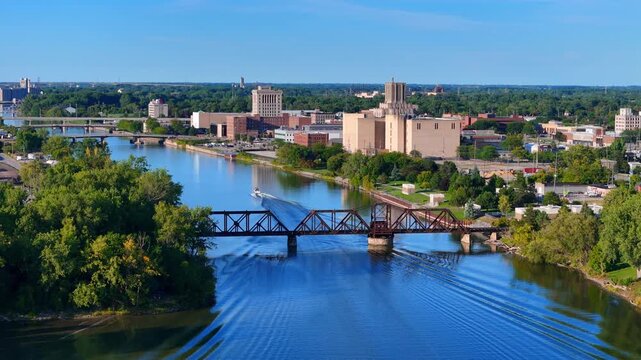 Saginaw River with a boat passing under a railway bridge, city buildings lining the waterfront