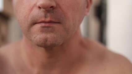 Naklejka premium Closeup white man finishing shave with calm expression, concentrating on lower face and jaw, small household background hints, scene evokes everyday grooming before leaving for daytime plans
