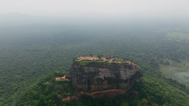 Sri Lanka drone orbit of Sigiriya Rock Fortress showing the flat summit ruins against a vast jungle horizon.