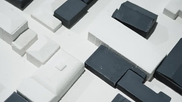 Close-up abstract arrangement of monochrome rectangular blocks forming a geometric architectural model with high-contrast textures, modular grid layout, and sculptural surfaces