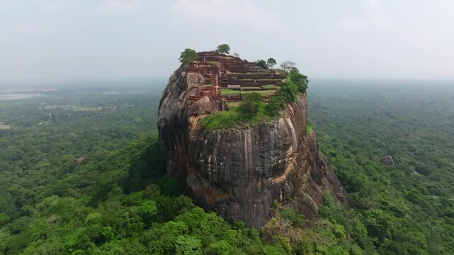 Sri Lanka drone wide shot of Sigiriya fortress perched on a towering monolith, with lush forest spreading to the horizon in every direction.