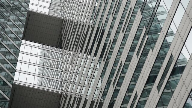 Diagonal view of modern glass skyscrapers linked by an elevated skybridge, with reflective curtain walls, repeating lines, and geometric patterns in an urban composition