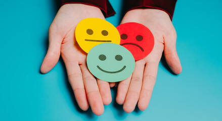 Feedback concept. Colorful emotion faces on paper held in hands, expressing happy, sad, and neutral...