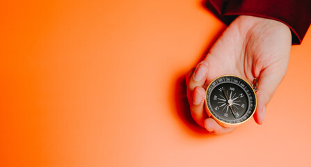 Hand holding compass on orange background, symbolizing direction and guidance with warm tone and clear focus