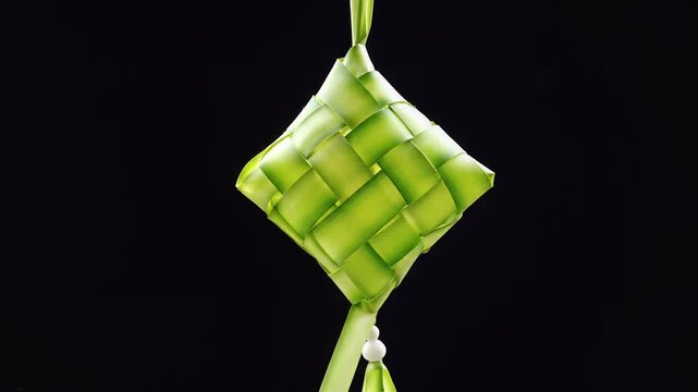 A single, intricately woven green ketupat, a traditional rice dumpling container or decoration, made from palm leaves, hanging against a dark background.