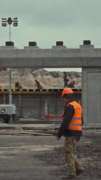 Construction contractors, clad in protective gear and safety helmets, actively work at a bustling building site surrounded by equipment and specialized clothing, adhering to stringent safety protocols