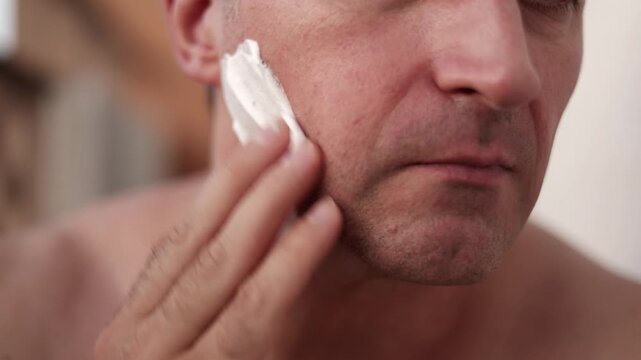 Men carefully applying moisturizing cream, Close proximity of man spreading cream delicately on face, Caucasian man carefully dabbs moisturizing cream on face with attentive expression during routine