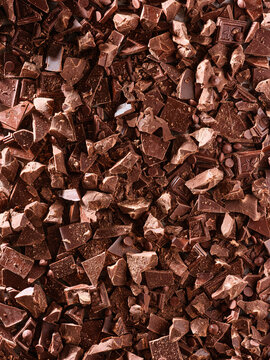 Different sizes of chocolate chunks and pieces are spread over a flat surface. These pieces are used for baking and cooking in various recipes