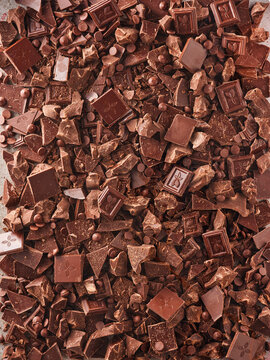 Different pieces and chips of chocolate fill a flat surface. The chocolate varies in shapes and sizes, ready for use in recipes or baking