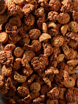 Cookies of various shapes and sizes are spread out on a dark surface. The warm light highlights the rich colors and textures of each cookie. This setup invites a closer look