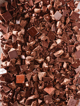 Chocolate is chopped into small pieces on a flat surface. These pieces are ready for use in baking or preparing desserts. They vary in size and shape, showing a mix of dark and light colors
