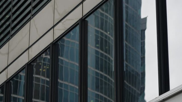 Close-up of a modern glass facade with vertical mullions reflecting a curving skyscraper, highlighting geometric patterns, lines, and architectural details across window panels.