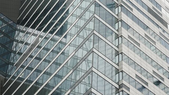 Close-up of a modern glass skyscraper facade with geometric zigzag lines, reflective windows, and steel structure, showcasing urban architecture and curtain wall design