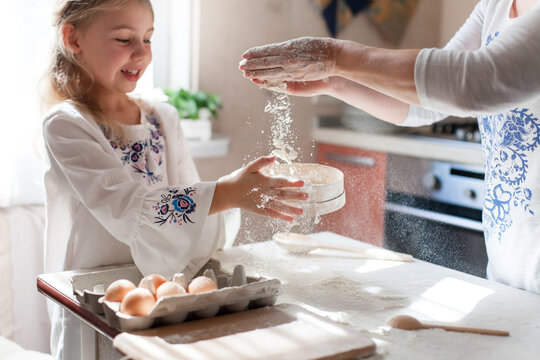 Flour flying as mother and daughter prepare Easter dough together. Playful spring baking moment with joy, family bonding. Slow cooking traditions. Authentic candid lifestyle, grandmacore.