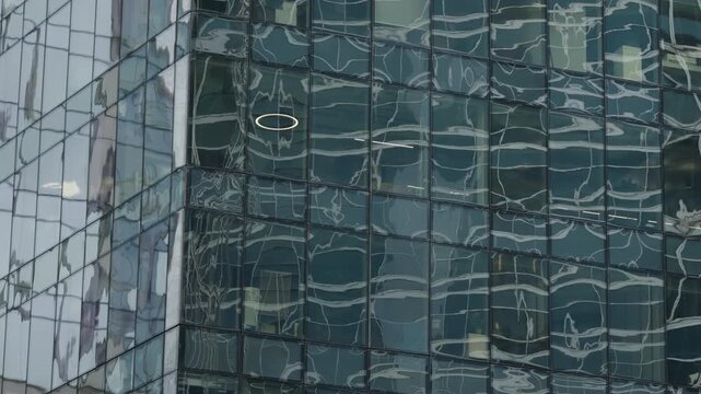 Abstract reflections ripple across the glass facade of a modern office skyscraper, revealing distorted patterns and a grid of windows that emphasize contemporary architecture