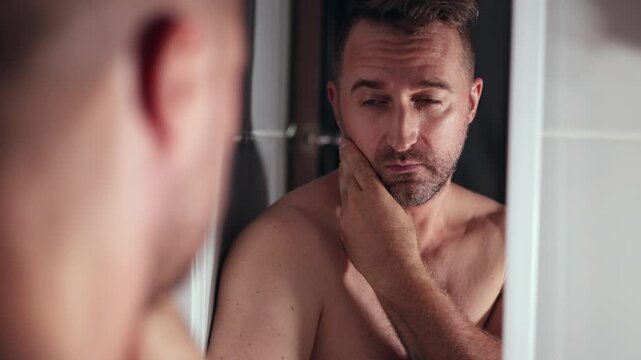 Concerned dad reflecting, Father inspecting face in mirror, Caucasian man examines his face with concern early morning, Father looks at himself anxiously in bathroom mirror during morning time