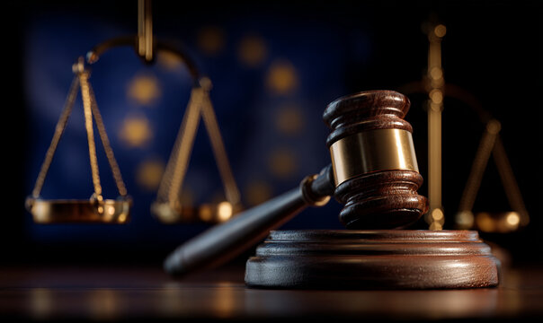A gavel rests on a sound block in front of the European Union flag and scales