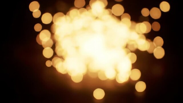 A mesmerizing video with a dolly and zoom out captures warm golden-toned luminous bokeh light particles coalescing into a pulsating cluster from a black void. Enchanting ambiance