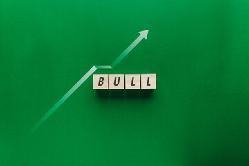 Top view of wooden blocks spelling BULL with a rising green arrow graph on a green background....