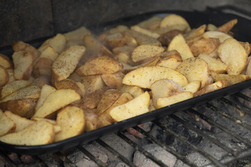 Potato wedges baking on barbecue grill in outdoor fireplace