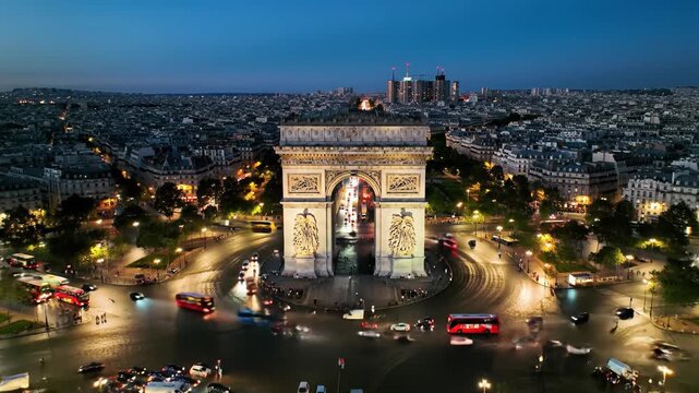 Aerial drone video of Arc de Triomphe and Place Charles de Gaulle at dusk transitioning to Parisian night. Golden lights, traffic streaks on wet asphalt. Magnificent urban romance