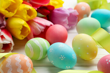 Fototapeta premium Painted Easter eggs and beautiful tulips on white wooden table, closeup