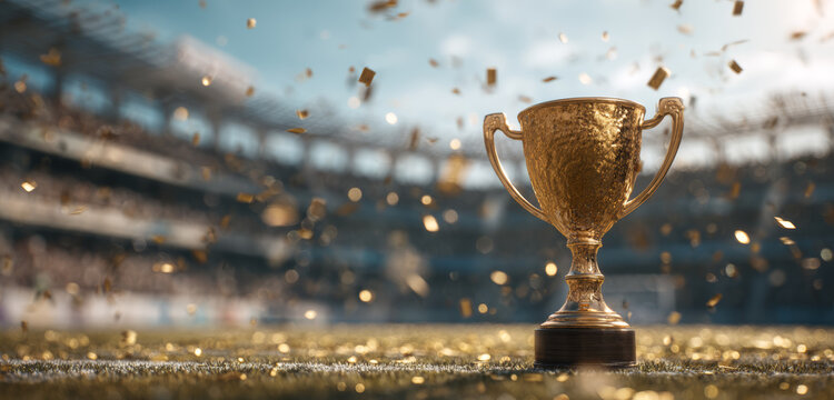 Golden trophy with textured surface and ornate handles placed on a football stadium field amidst colorful confetti during an award ceremony