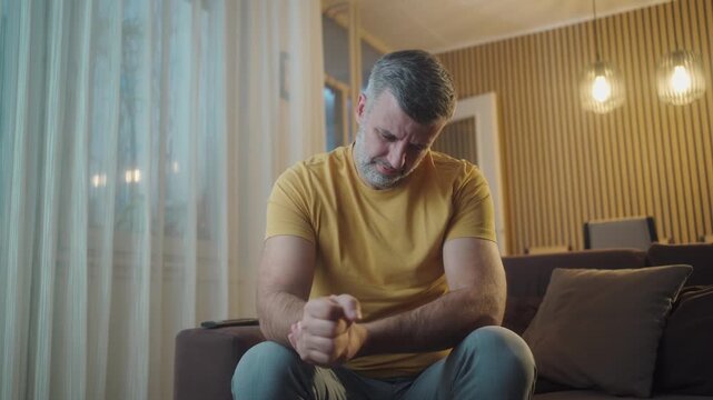 Handsome man massaging painful wrist after working on laptop at home, suffering from numbness