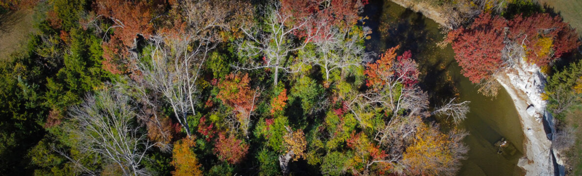 Panorama aerial view dense woodland at Anderson Bonner Park with curved White Rock Creek flows through west Hillcrest Rd, Park Central Dr. Dark water, scattered rocks, fiery foliage, Dallas, TX