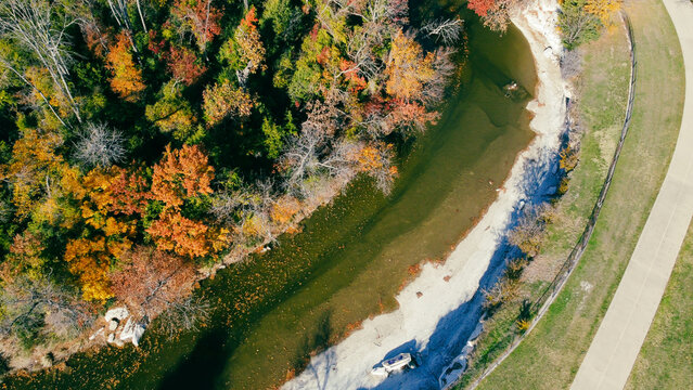 White rocky shoreline of White Rock Creek near Churchill Way curves past pale bank east of Hillcrest Rd. Shallow water, exposed riverbed, vivid foliage blend textured fall scene, Dallas, Texas