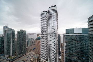 Naklejka premium Toronto downtown cityscape showcasing a dense cluster of contemporary skyscrapers, residential towers, and corporate offices lining the urban waterfront under a cloudy sky. In mimco