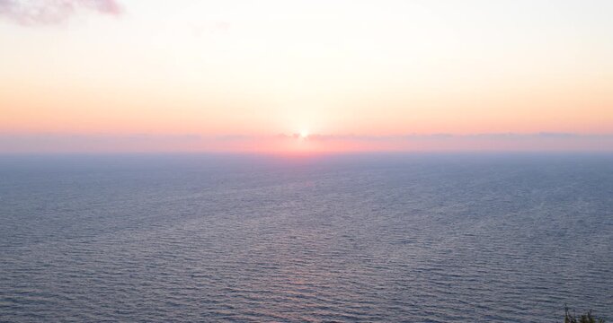 Sonnenaufgang &uuml;ber ruhiger Meeresfl&auml;che mit klarer Horizontlinie, erste Sonnenstrahlen steigen langsam aus dem Wasser auf, sanfte Farbverl&auml;ufe am Himmel und stille Morgenstimmung &uuml;ber dem Meer