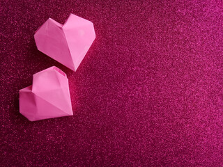 Two pink origami hearts shape on glitter background.
