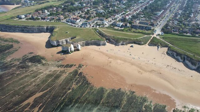 Drone aerial view of coastline of Margate town with sandy beach meeting the atlantic ocean. Waves create patterns over dark rocks and green algae.  Kent United Kingdom